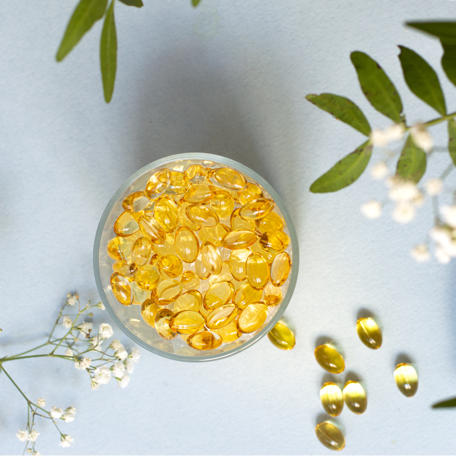 Gelbe Omega-3-Kapseln in Glasschale auf hellem Hintergrund, symbolisieren essentielle Fettsäuren für Gesundheit und Leistungsfähigkeit