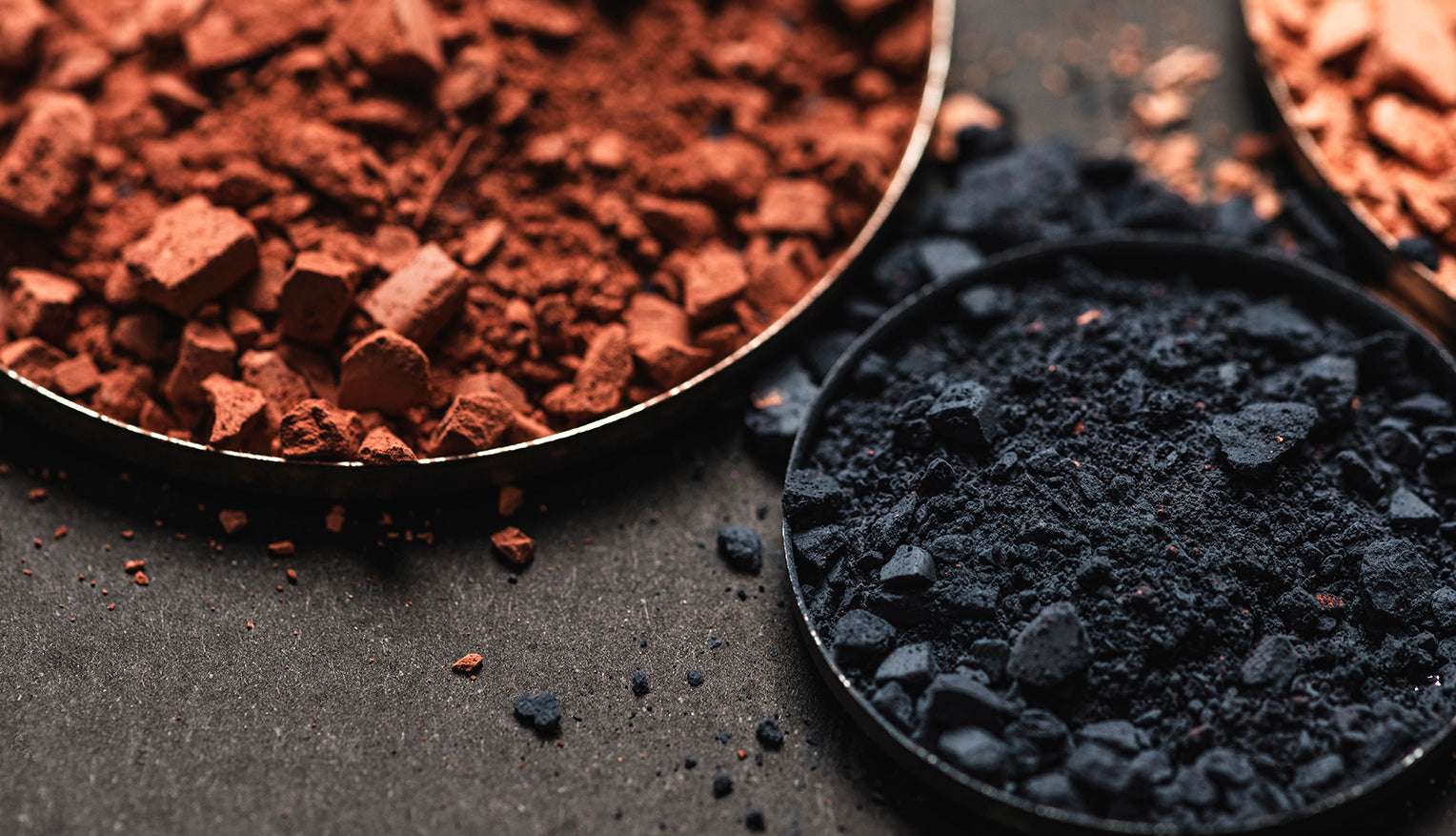 Shilajit-Pulver in einer Metallschale, daneben rötliche Mineralstücke auf dunkler Oberfläche.