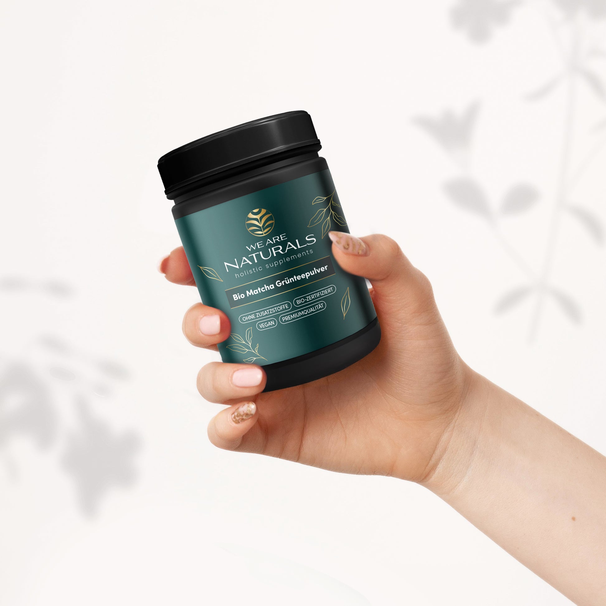 Bio Matcha Grünteepulver von We Are Naturals – Produktdose in einer Hand gehalten vor hellem Hintergrund mit Pflanzenillustrationen